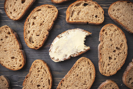 Top view of sliced whole grain bread with a buttered piece, on a rustic wooden background