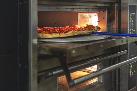 Delicious pepperoni pizza on a metal peel, sliding into an industrial oven with a warm glowの写真素材