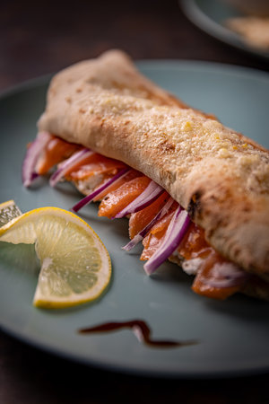 Delicious closed calzone pizza with salmon, cream cheese, red onions and lemon slices on elegant...