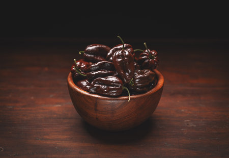 Chocolate habanero peppers overflowing a wooden bowl, sitting on a dark, rustic wooden tableの写真素材