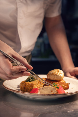 Professional chef adding finishing touches to a plated gourmet meal, sprinkling crumble topping in a restaurant kitchenの写真素材