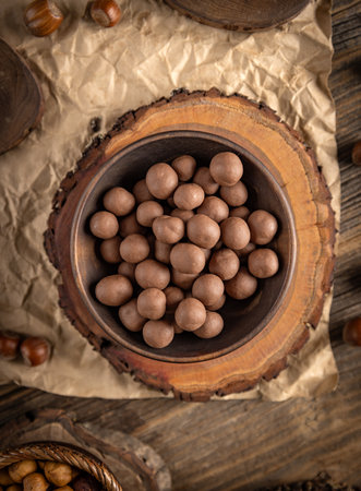 Chocolate covered hazelnuts are displayed in a bowl on a wooden stand, creating a tempting treatの写真素材