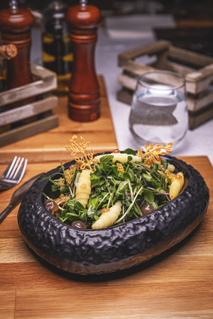 Gourmet green salad with pears and croutons served in black bowl on wooden tableの写真素材