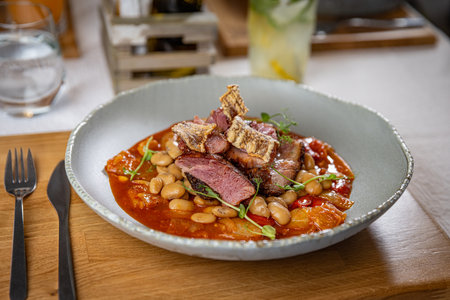 Roasted pork knuckle of ham with white beans, crispy pork skin, and tomato sauceの写真素材