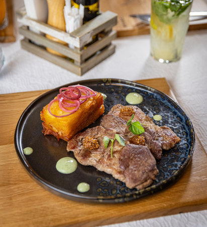 Grilled pork with potato gratin, decorated with red onion rings and mustard seeds, served on a dark plateの写真素材