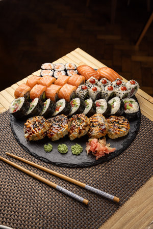 Sushi platter with various rolls, nigiri, and wasabi displayed on slate with chopsticksの写真素材