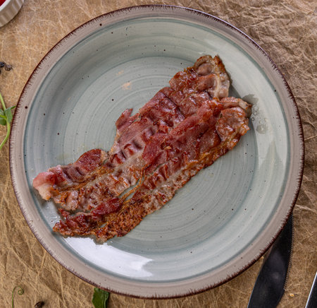 Fried bacon piece for breakfast or a side dish on an artisan plateの写真素材