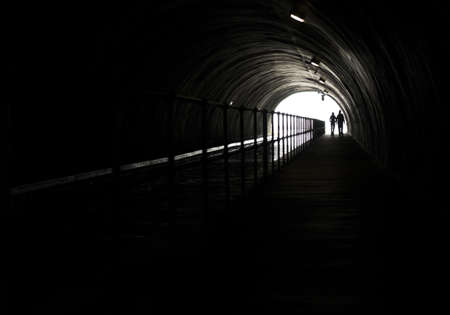 Silhouette Of A Couple In Front Of Bright Light At The End Of A Dark Tunnelの写真素材