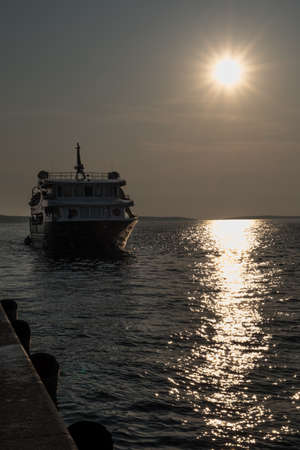 Ferry Boat Retourns Into Harbor In The Evening With Bright Shining Sunの写真素材