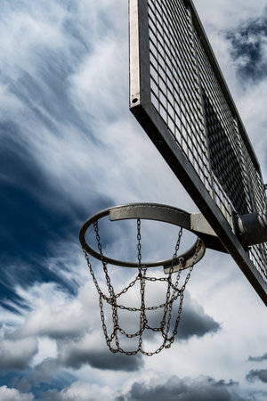 Metal Basketball Board And Ring With Chains In Front Of Sky With Heavy Cloudsの写真素材