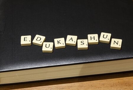 Game letter tiles purposely mis-spelling edukashun arranged on bookのeditorial素材