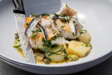 prepared dish of pan fried cod with whitebait capers courgette and garnish with serrated knifeの写真素材