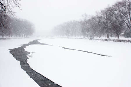 Tree lined river with small area of dark water mostly covered with ice and snow in winter.の写真素材