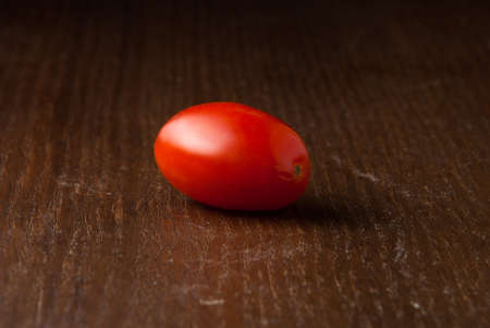 One single red cherry tomato on a wood tableの写真素材