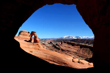 The world famous Delicate Arch in Arches National Park / USA on a sunny day with a clear blue sky - Shot from caveの写真素材