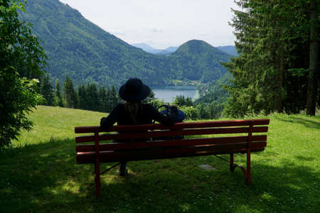 Sporty hiker woman takes a break on a bench and enjoys the view onto a lakeの写真素材