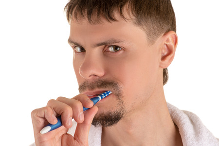 Portrait of serious adult man with white towel on his shoulders looking at camera and cleaning teeth white and blue toothbrushの写真素材