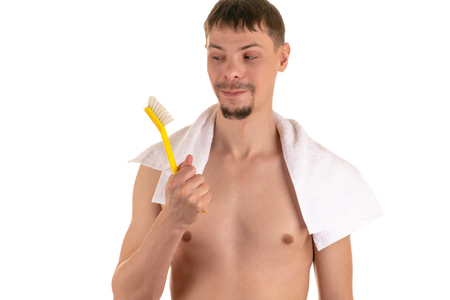 smiling adult naked man looks at big bright yellow toothbrush in his right hand and white towel on his shouldersの写真素材