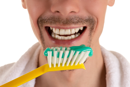 lower part of face of man with big yellow toothbrush and white towel on shoulders closeupの写真素材