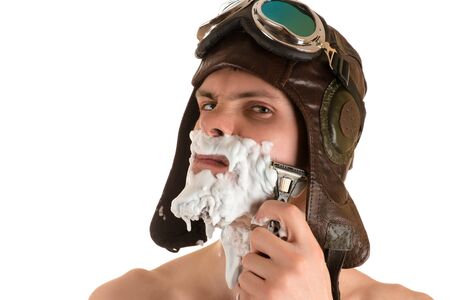 portrait of man shaving with shaving foam on his face in flight helmet and flying goggles looking sternly at cameraの写真素材