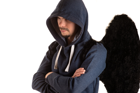 young man in gray jacket with hood thrown over his head with his arms folded and black wing of left shoulderの写真素材