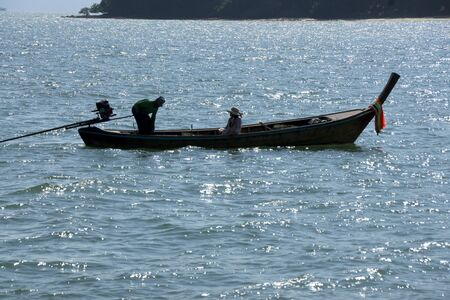 man and woman in long fishing boat with motor in oceanの写真素材