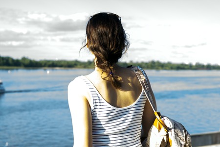 Young lonely girl with a backpack standing on the coast of the river hot summerの写真素材