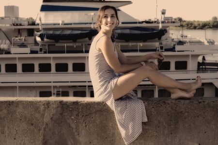 Sexy girl sits on a wharf and looking up on a background of ship, Color filtered effectの写真素材