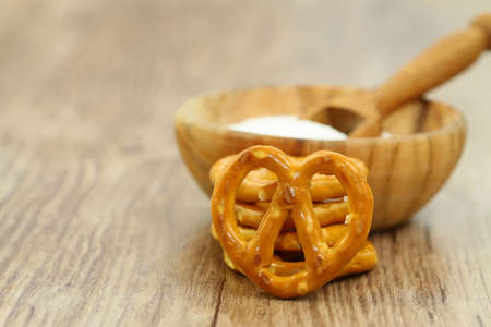 Salty pretzel leaning against stack of pretzels and wooden bowl with saltの写真素材