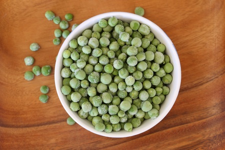 Frozen green peas in bowl on wooden surfaceの写真素材