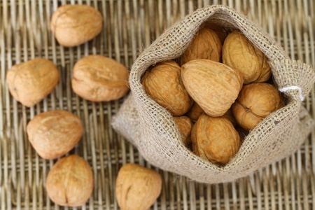 Whole walnuts in jute bag on wicker background, close up