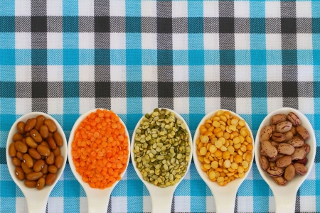 Selection of pulses on porcelain spoons on checkered tablecloth with copy space