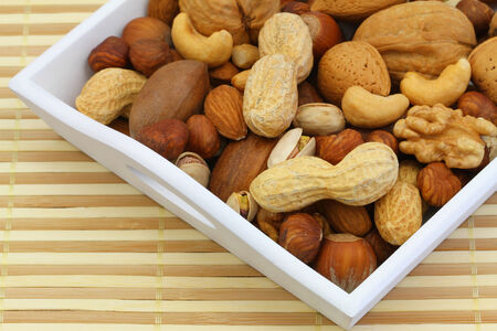 Selection of nuts on white wooden tray on bamboo matの写真素材