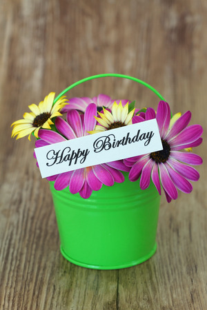 Happy Birthday card with pink and yellow daisies in green bucketの写真素材
