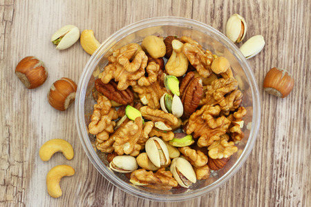 Selection of mixed nuts in plastic box on wooden surfaceの写真素材