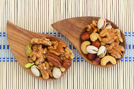Selection of mixed nuts in wooden bowls on bamboo matの写真素材