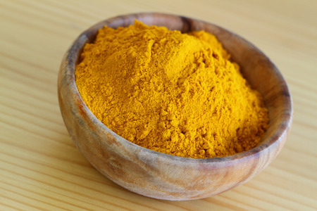 Tumeric powder in wooden bowl, close upの写真素材