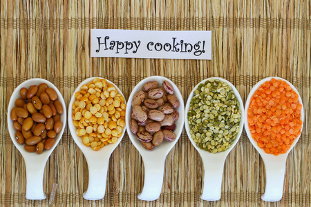 Happy cooking card with selection of pulses on porcelain spoons on bamboo matの写真素材
