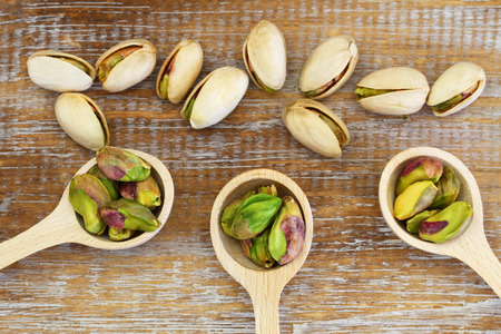 Pistachio nuts on wooden spoons on wooden surfaceの写真素材