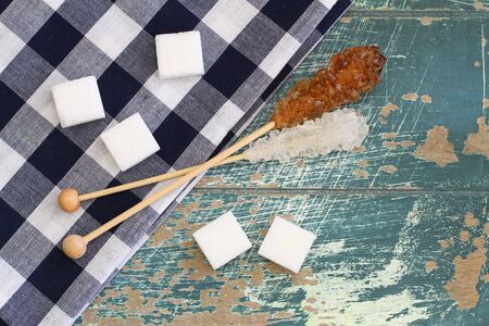 White sugar cubes and white and brown sugar sticks on rustic wooden surface