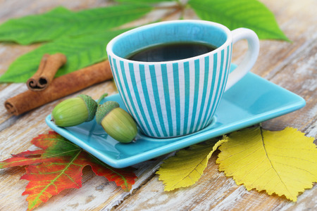 Coffee in vintage cup and autumn leaves and acorns on rustic wooden surfaceの写真素材