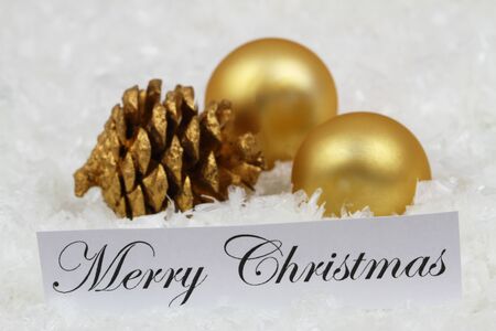 Merry Christmas card with golden baubles and pine cones on snowy surfaceの写真素材