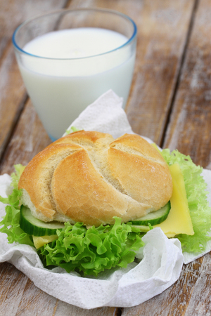Cheese roll with lettuce and glass of milk on rustic wooden surfaceの写真素材