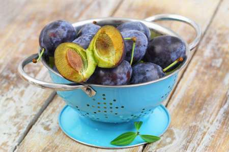 Fresh plums in blue colander on rustic wooden surfaceの写真素材