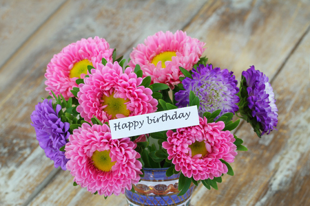 Happy Birthday card with colorful aster flower bouquet on rustic wooden surfaceの写真素材