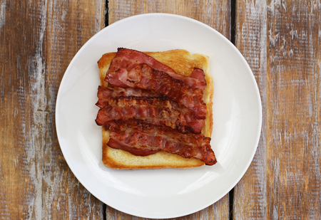 Crispy bacon on toast on white plate on rustic wooden surfaceの写真素材