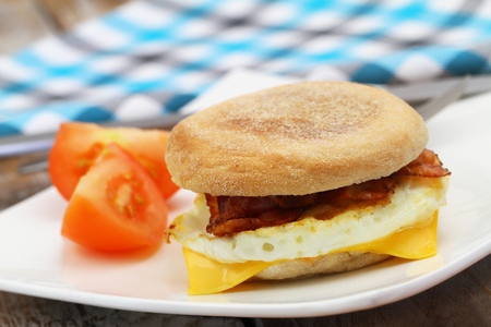 Egg and bacon muffin on white plate with slices of tomato on the sideの写真素材