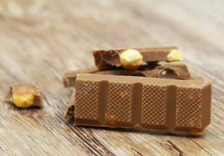 Milk chocolate pieces with whole hazelnuts on rustic wooden surface with copy space