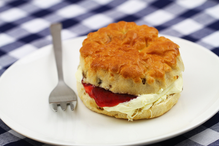 Scone with raisins with traditional clotted cream and strawberry jam on white plateの写真素材