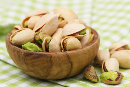 Pistachios in wooden bowl on green and white checkered cloth, closeupの写真素材